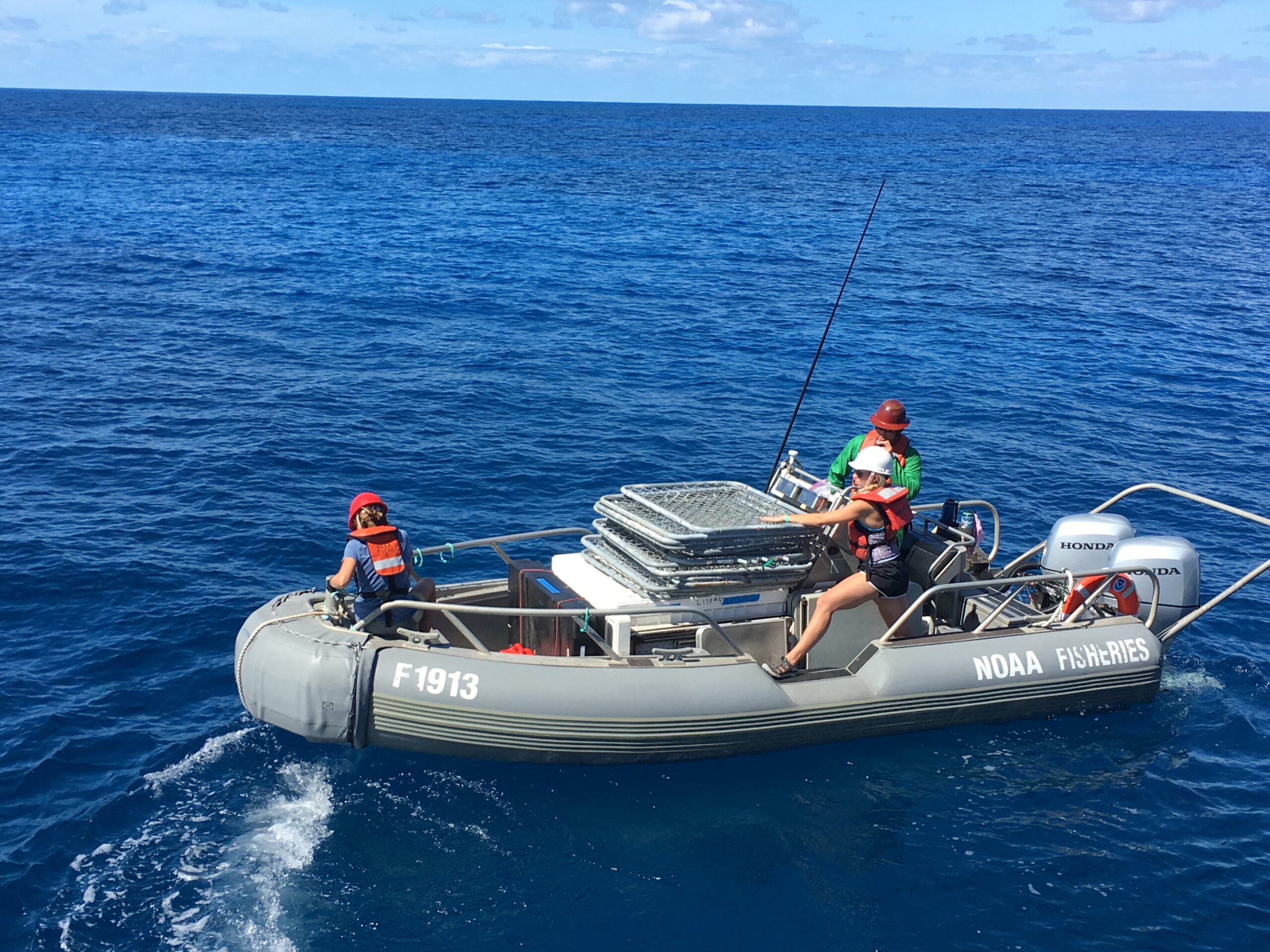 Three workers on a small gray boat in a deep-blue sea