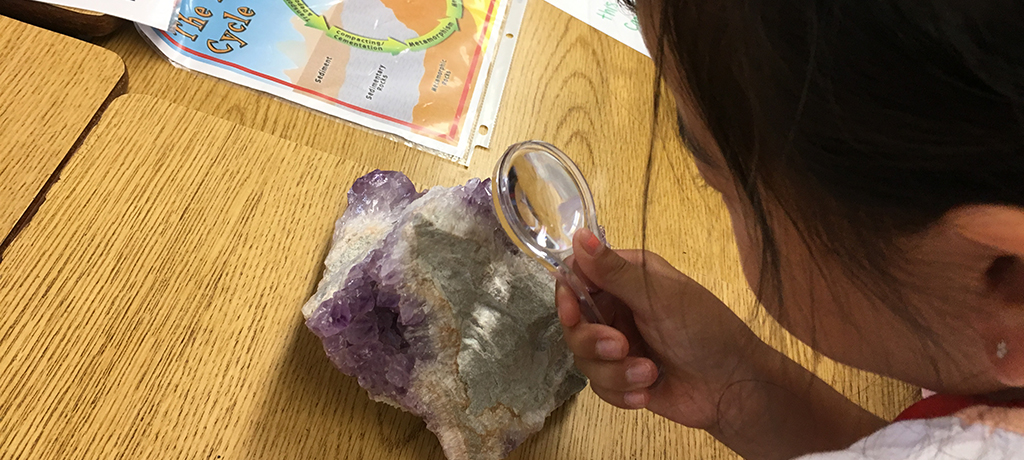 student inspecting rock with magnifying glass