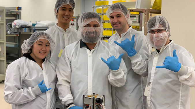 Five members of the Hawaii Space Flight Lab team, in lab coats, gloves and hairnets.