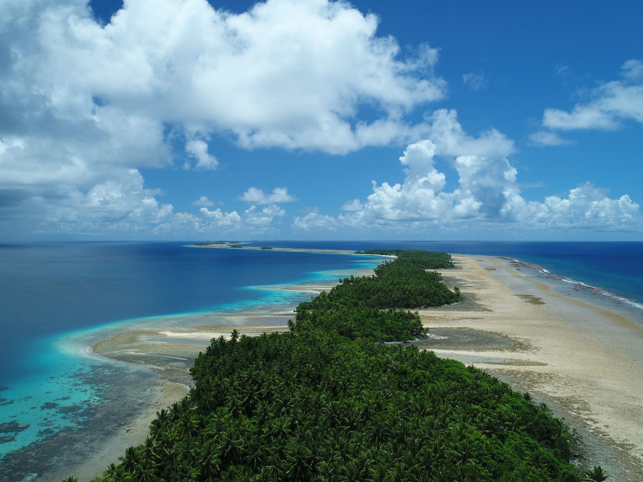 Low-lying windward reef islands of Majuro atoll. A narrow strip of vegetation is visible in the middle of a low, narrow island