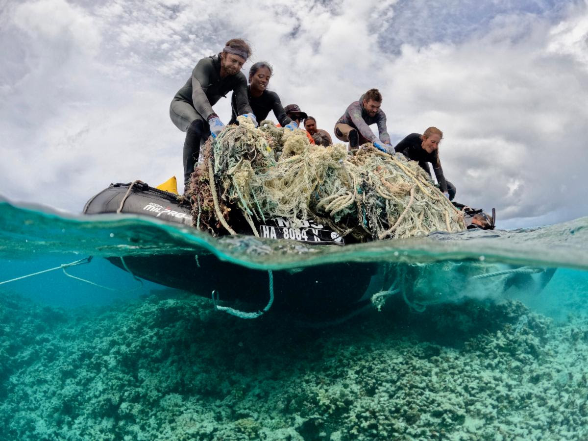 Divers work together to remove a large ghost net from the shallow coral reef environments of Kamokuokamohoali'i (Maro Reef)