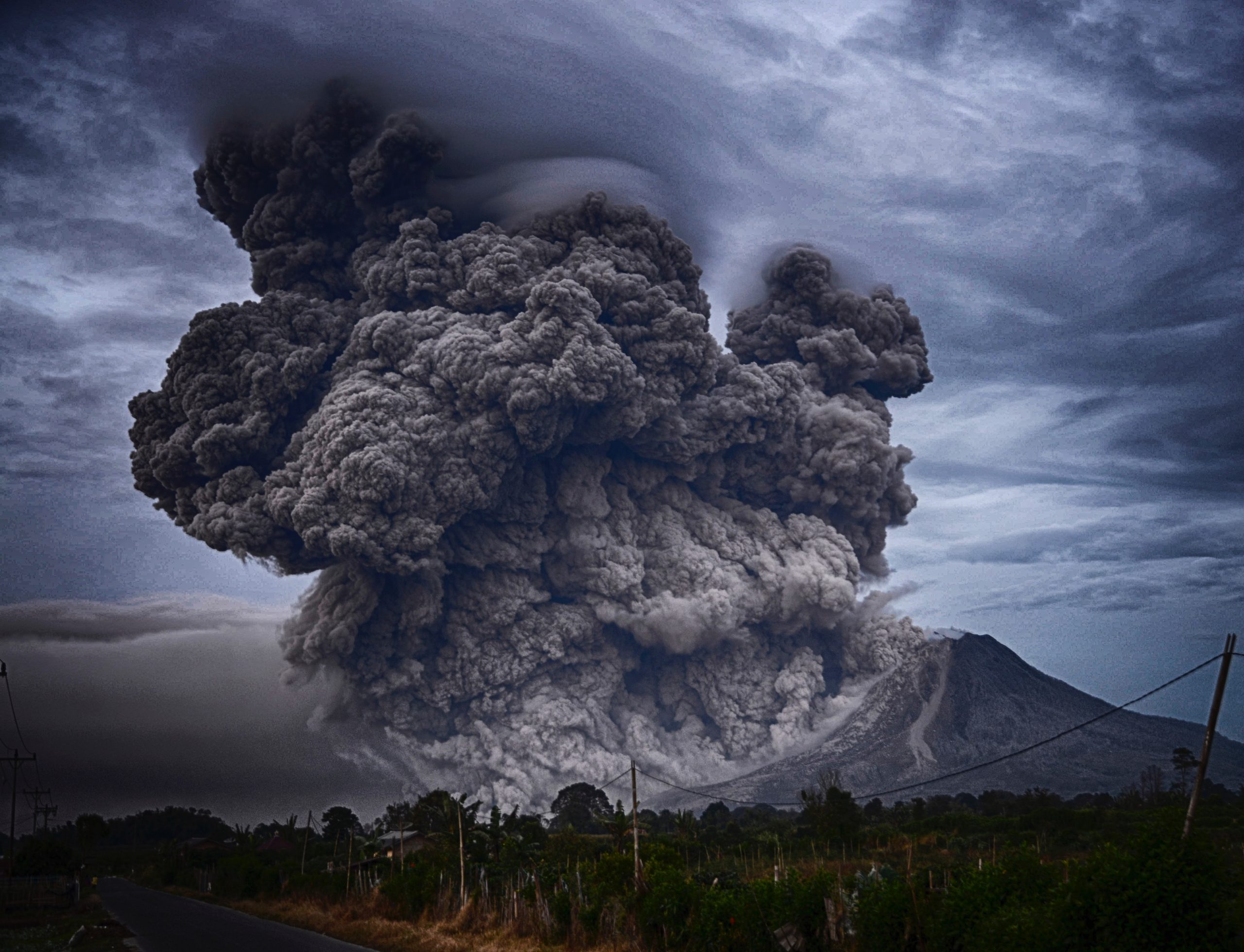 Mount Sinabung (volcano) in Indonesia erupts with a huge smoke and debris cloud. Cloudy skies are behind the volcano.