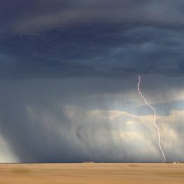 Large rain storm over plains with lightning bolt striking the ground.