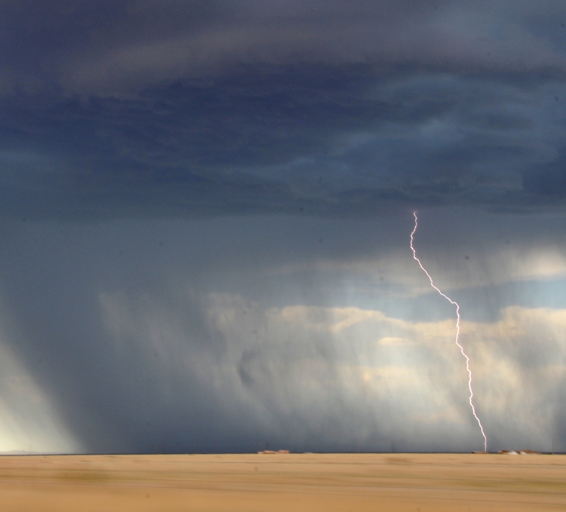 Large rain storm over plains with lightning bolt striking the ground.