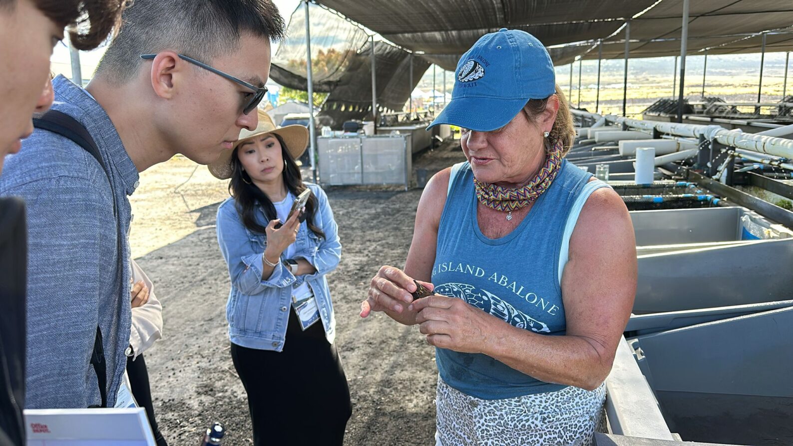 At a farm tour of Big Island Abalone, someone from the company shows two visitors an abalone.