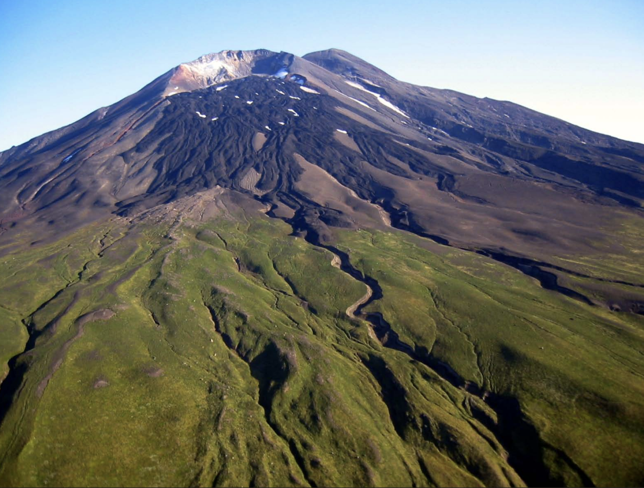 Mount Gareloi, Aleutian Islands. Foreground section of the volcano is green. Background peak is dark with small patches of snow.