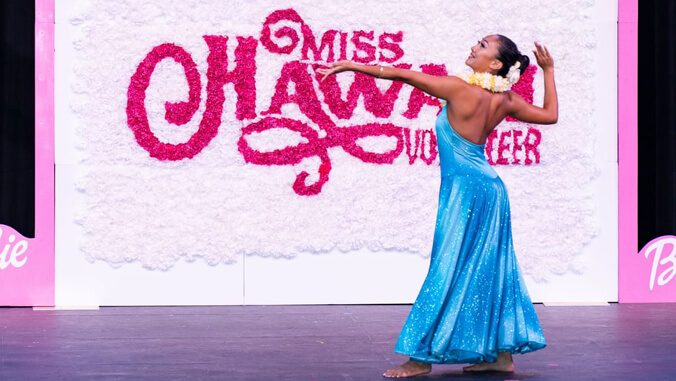 Makenna Kinsler dancing on a stage in front of a sign that reads "Miss Hawai'i Volunteer"