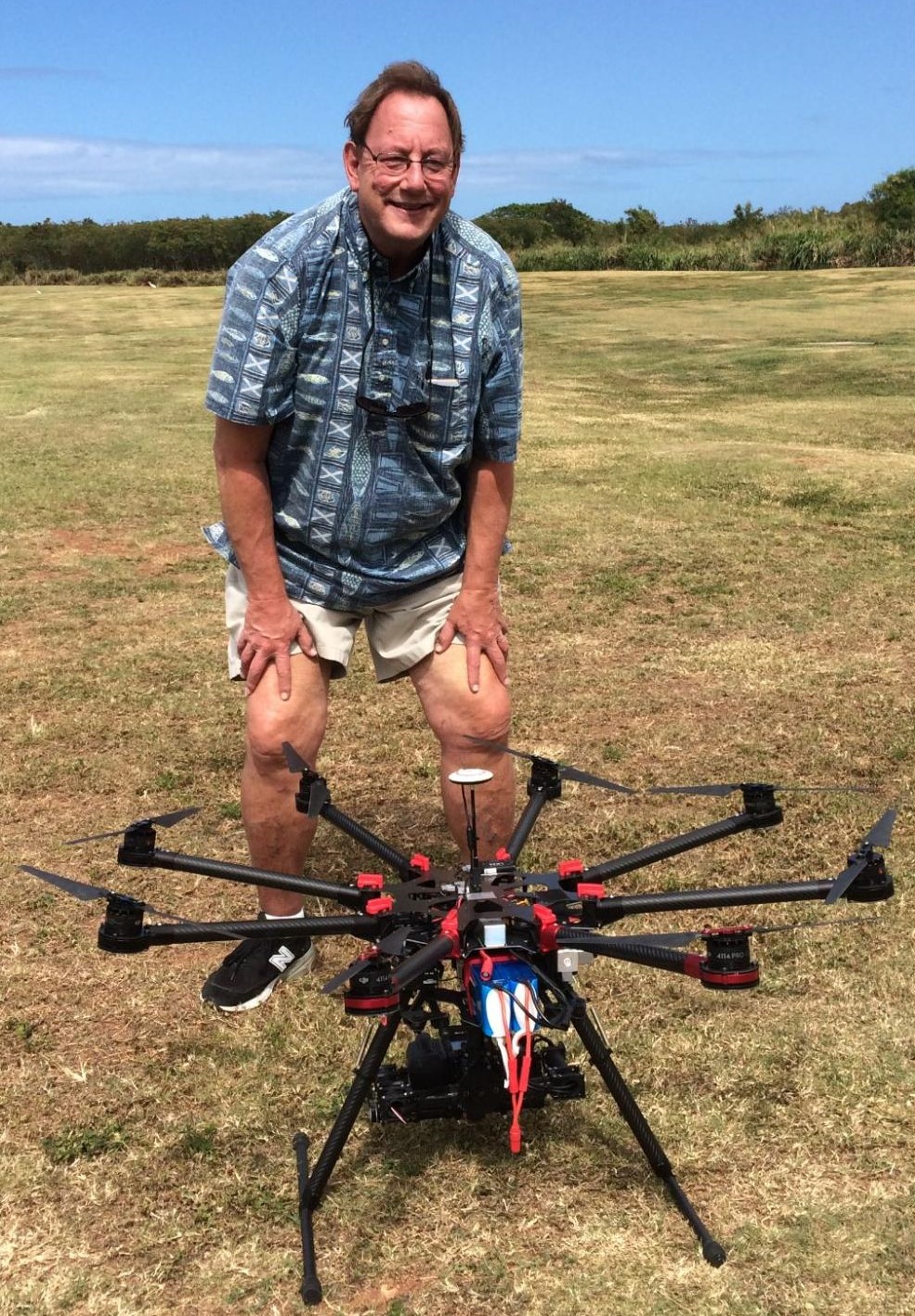 Craig Glenn stands in a field by a black and red thermal imaging UAV/ drone.