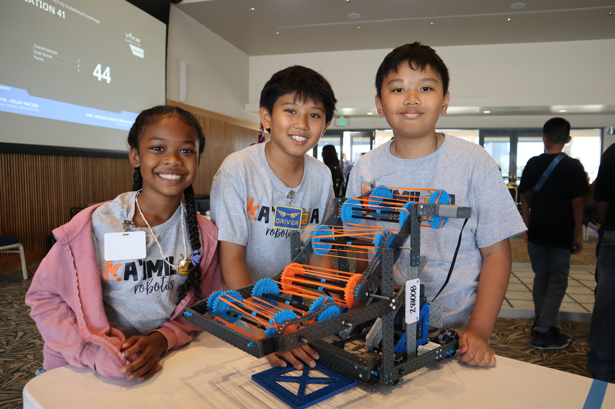 Three elementary student competitors stand, smiling, at a table with their robot.