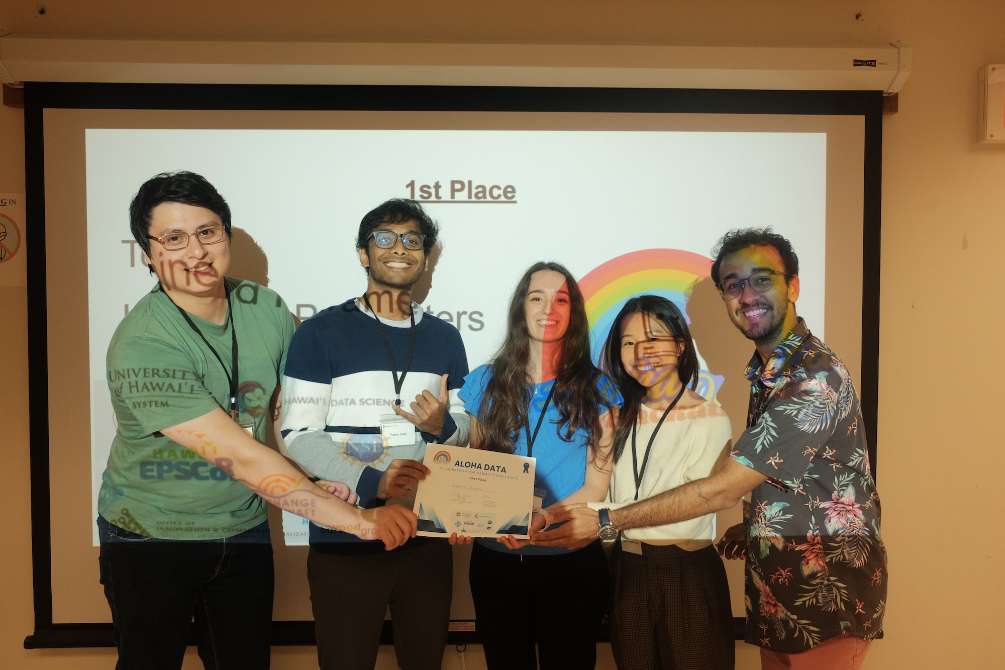 Five students, smiling, all hold a first place certificate in front of a projector screen.